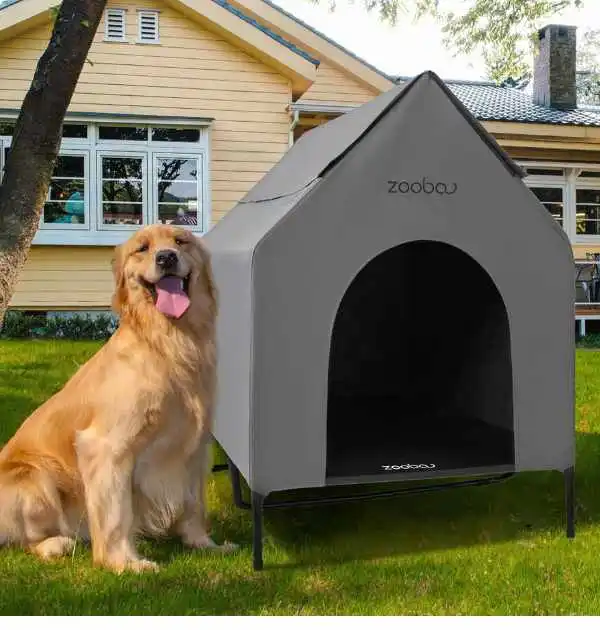 A golden retriever sitting beside a gray insulated outdoor dog house labeled "Zooba," set in a grassy yard with a house in the background.